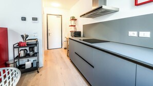 Et moderne køkken med lysegrå skabe, en sort bordplade og et rustfrit stål stinkende emfang. Der er en lille hylde med en plante og et billede i rød ramme på væggen.