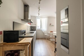 A compact kitchen with a microwave, stove, and sink. There is a dining area with a table and chairs. - L'Angolo d'Estella (Trieste)