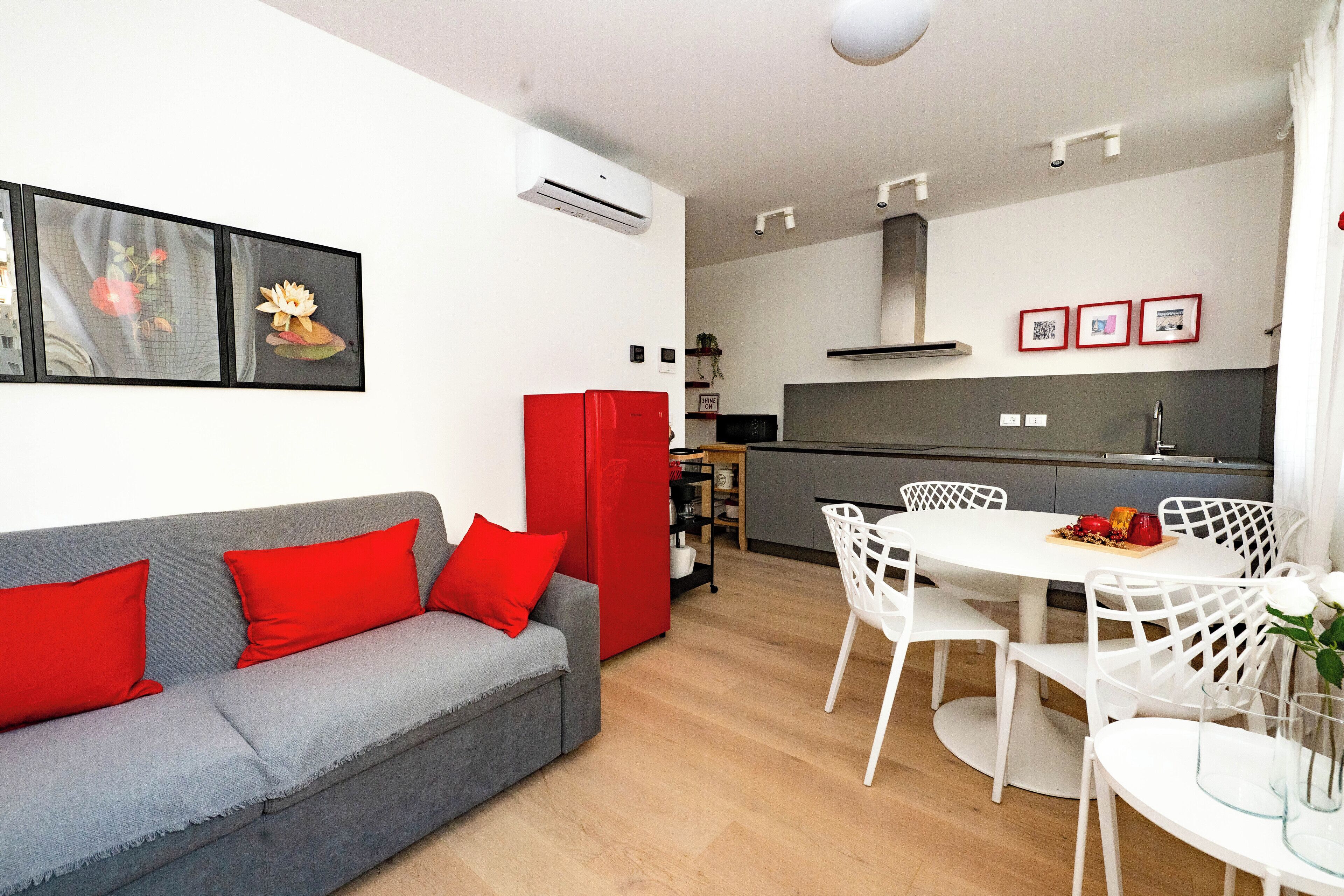 Un espace de vie moderne avec un canapé gris, des coussins rouges, une table à manger blanche et des chaises blanches.