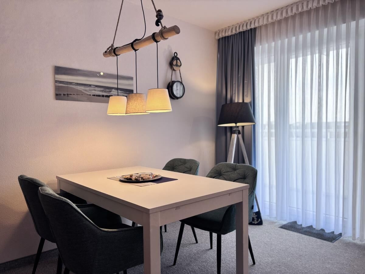 Una habitación de hotel con una mesa de comedor, cuatro sillas, una lámpara y un ventanal con cortinas.
