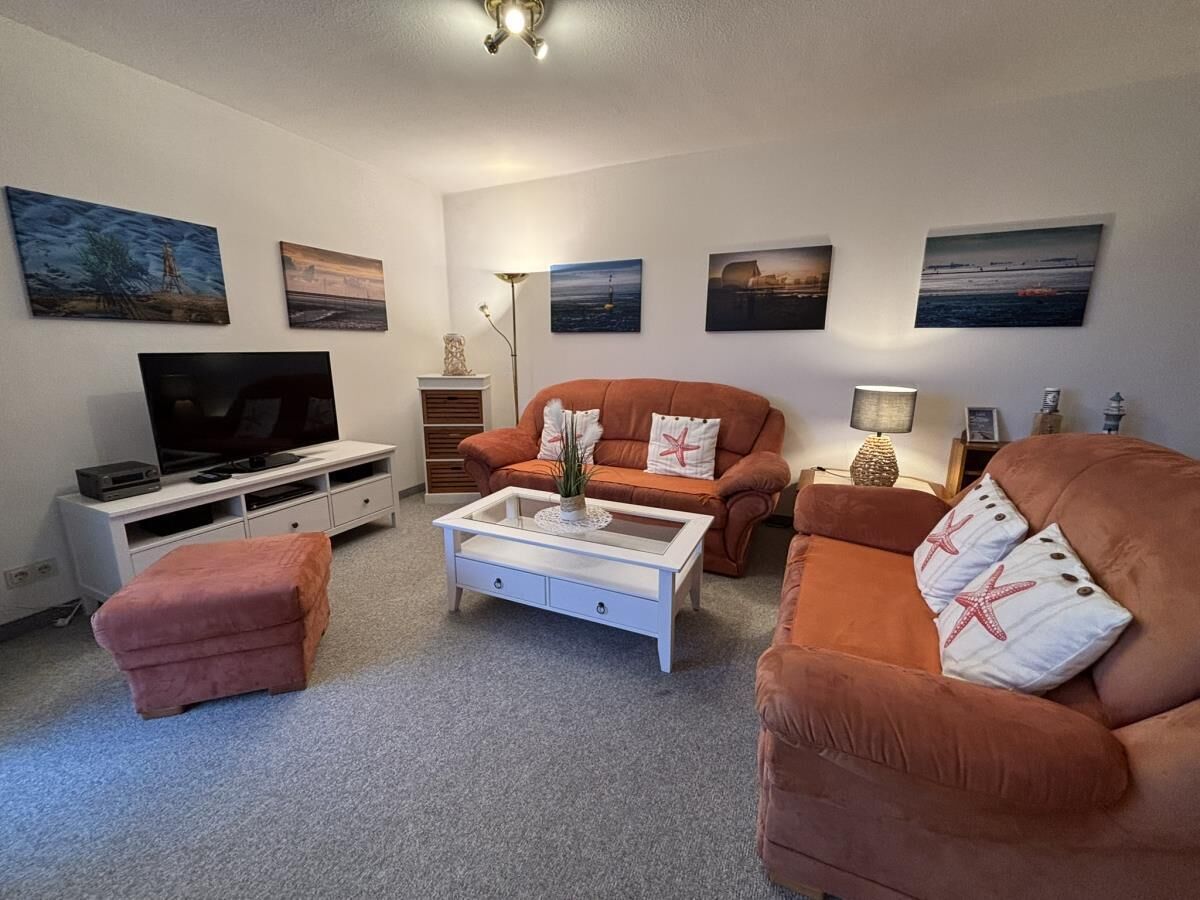 A living room with a flat-screen TV, a coffee table, two sofas, and a small ottoman.