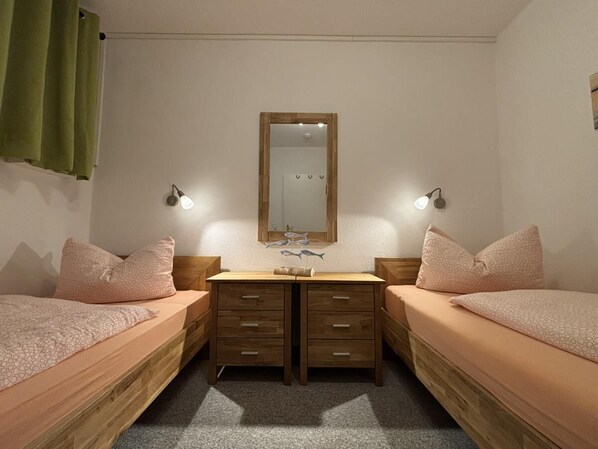 Ein Doppelzimmer mit zwei Einzelbetten, einer Holzkommode mit Schubladen, einem Spiegel über der Kommode und zwei Wandleuchten.