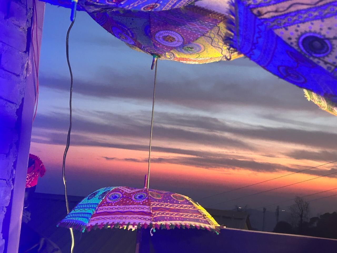 A colorful umbrella hanging indoors with a sunset view outside.