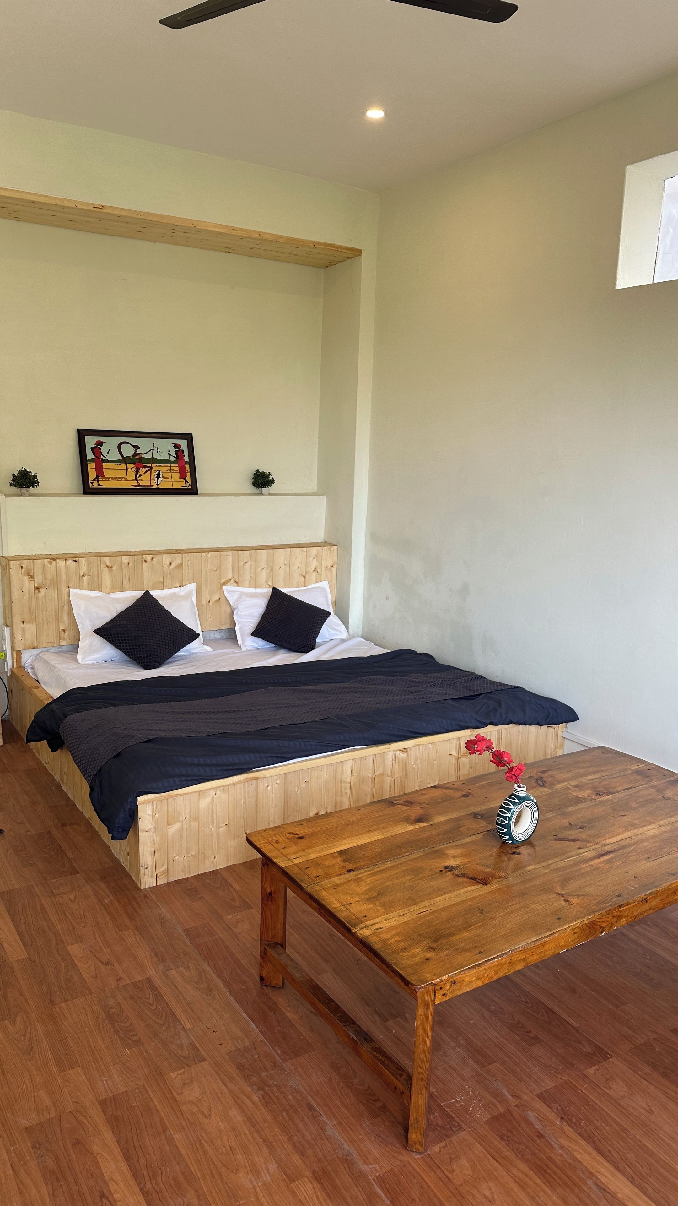A bedroom with a wooden bed, a nightstand, a wooden table with a vase, and a ceiling fan.