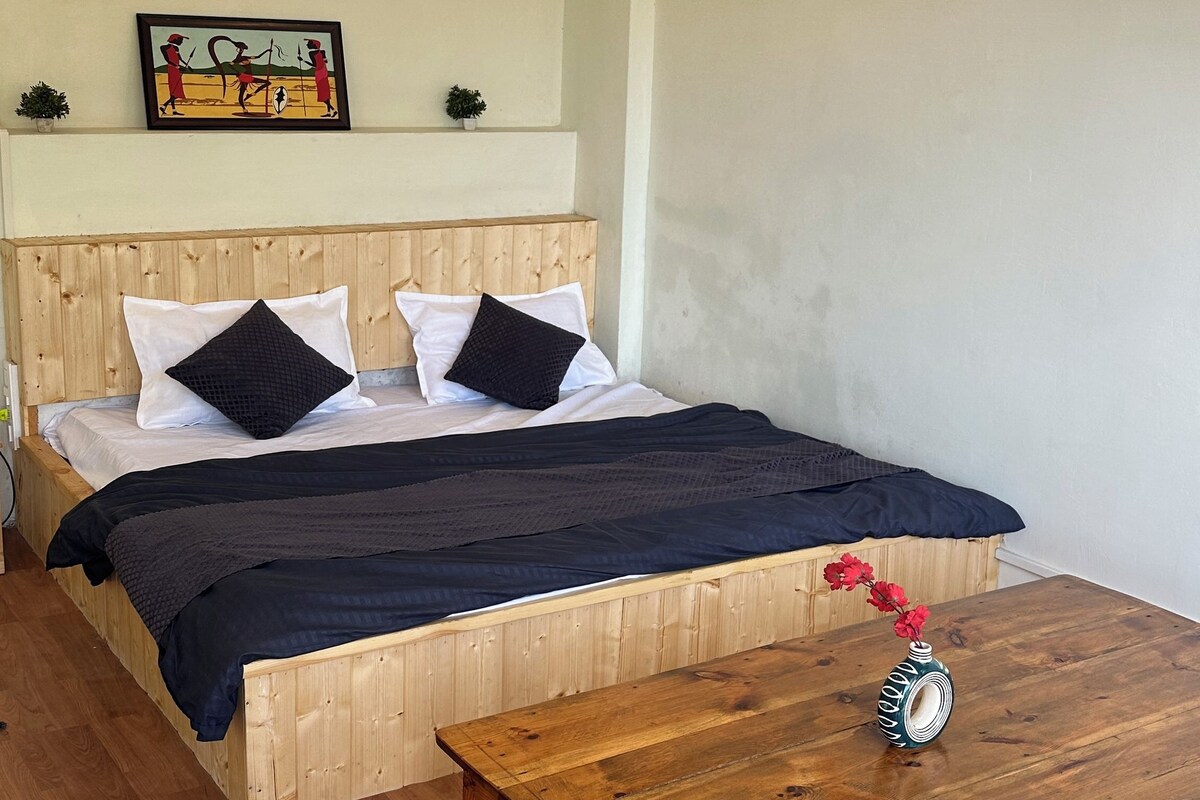 Une chambre à coucher avec un lit en bois, une table de chevet, une table en bois ornée d’un vase et un ventilateur de plafond.