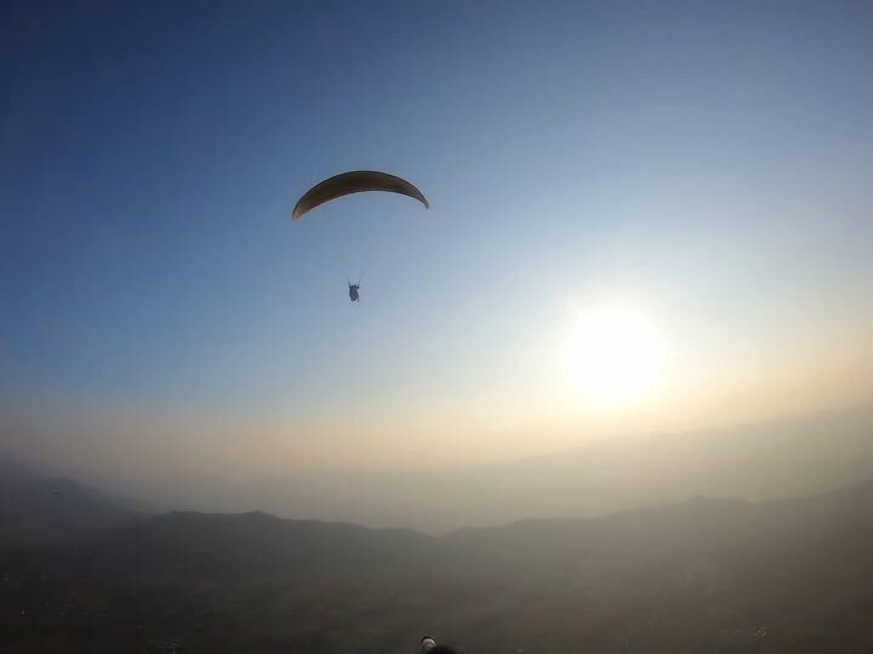 A person paragliding over a mountainous landscape with a clear sky.