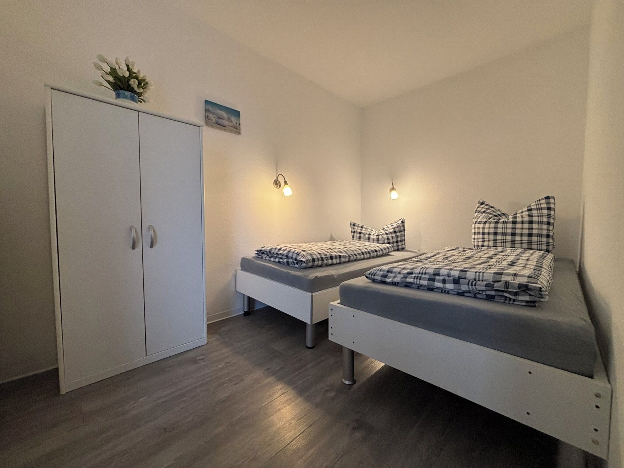 A bedroom with two beds, a wardrobe, and wall-mounted lights.