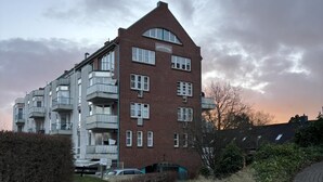 En fleretagers murstensbygning med altaner, med teksten "PAVILLON" og en parkeringsplads foran.