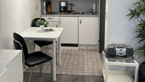Et kompakt køkken med lyse skabe, en mikrobølgeovn, kaffemaskine og spiseplads med bord og stole.