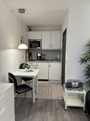 A compact kitchen with white cabinets, a microwave, a coffee maker, and a dining area with a table and chairs. - House Pavillon, vacation apartment HP13 (Cuxhaven)
