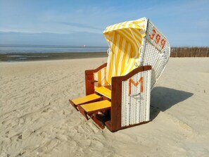 Uma cadeira de praia com guarda-sol listrado em uma praia de areia.