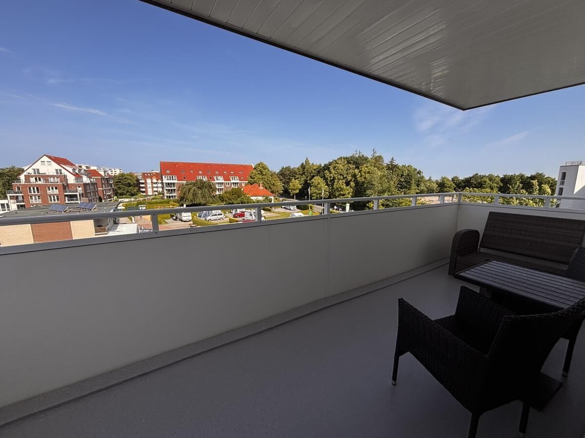 A balcony with a table and chairs, overlooking a residential area with buildings and trees.
