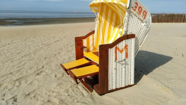 Ein Liegestuhl mit einem gestreiften Sonnendach am Sandstrand.