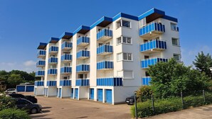 Ein mehrstöckiges Gebäude mit Balkonen, einem Parkplatz und blauem Himmel.