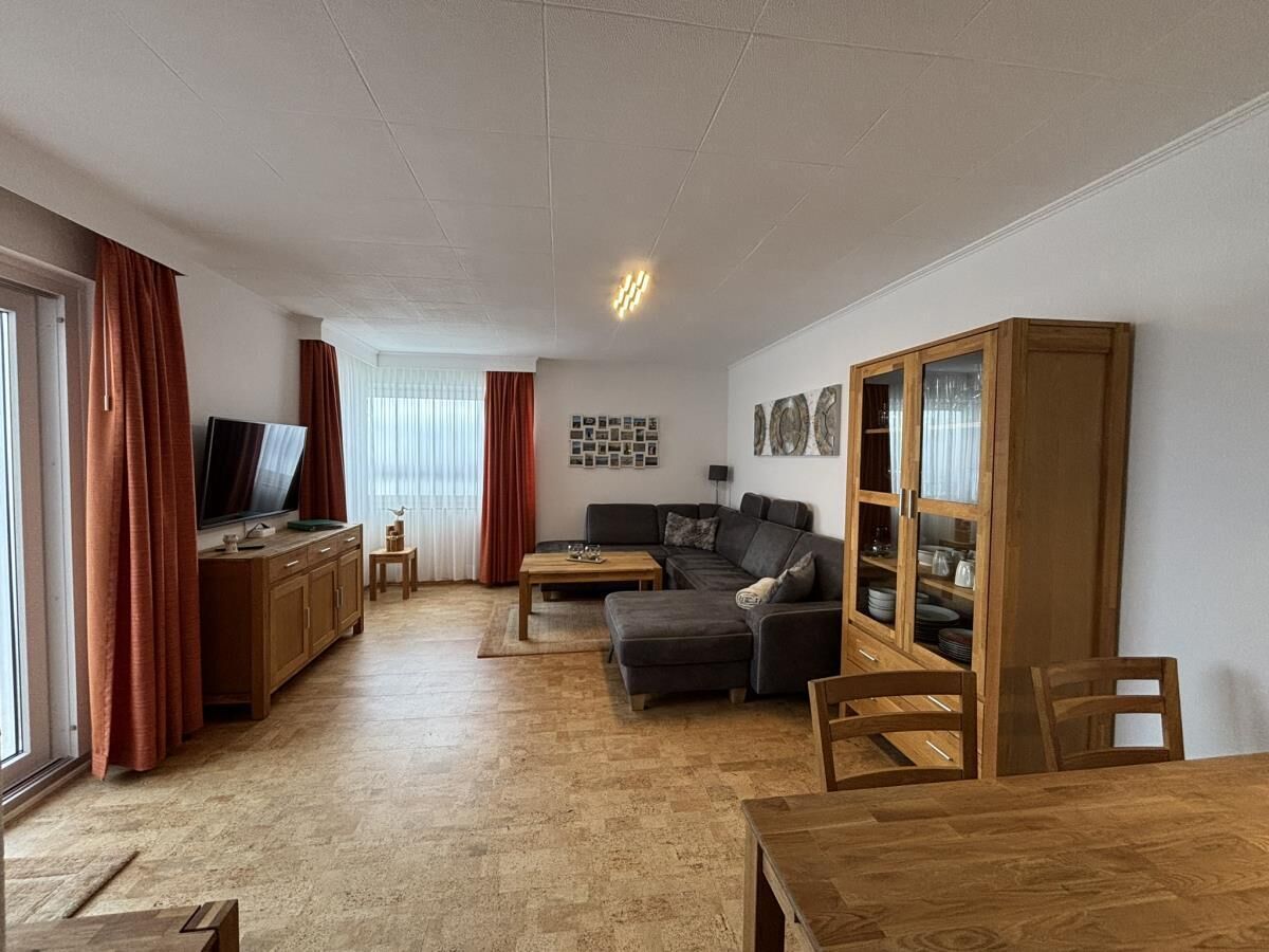 En stue med sofa, sofabord, fjernsyn, træskab og gardiner.