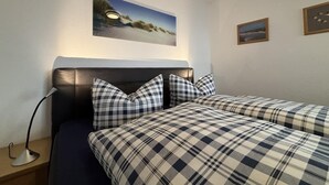 Ein Schlafzimmer mit dunklem Lederschlauchbett, zwei Betten mit Karomuster-Bettwäsche, einer Nachttischlampe und einem gerahmten Bild an der Wand.