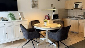 Moderni keittiö, jossa on ruokailutila, valkoiset keittiökaapit, litteänäyttöinen televisio ja seinällä oleva kello.