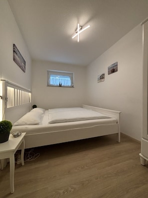 Ein Schlafzimmer mit einem Einzelbett, einem kleinen Tisch, einem Fenster mit Vorhängen und einer Deckenleuchte.