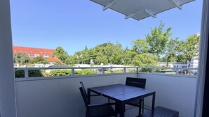 Parvekkeella on pöytä ja tuolit, valkoinen katto ja näkymä rakennuksiin ja puihin.