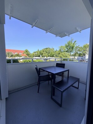 A balcony with a table and chairs, a white ceiling, and a view of buildings and trees. - House Poseidon, Apartment POS03 (Cuxhaven)