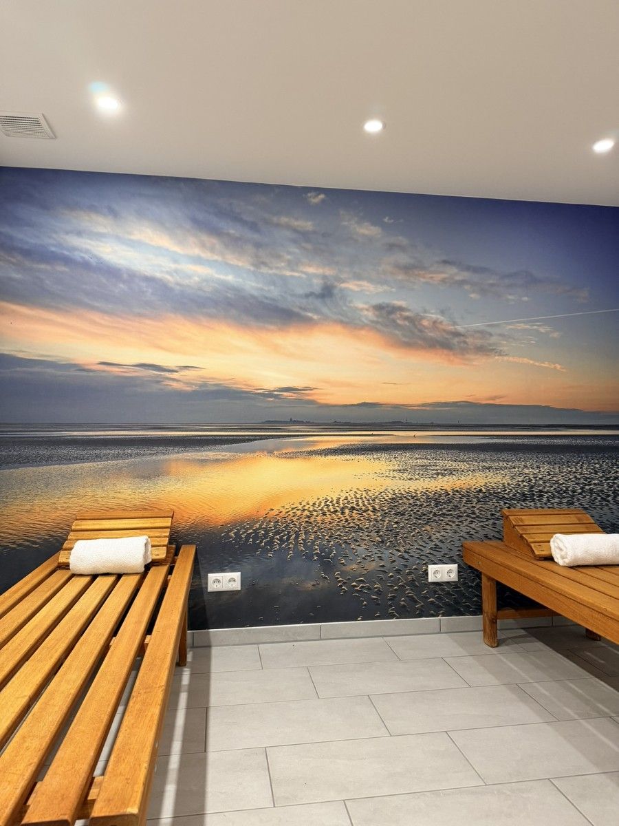 Una habitación con un mural de un atardecer sobre el agua, dos bancos de madera y un piso de baldosas.