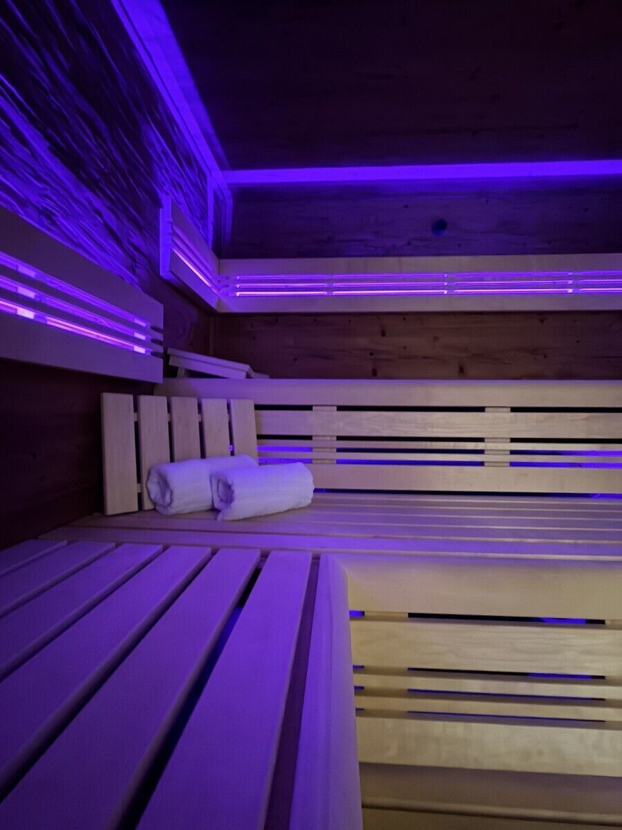 A sauna room with wooden benches and benches, purple lighting, and a towel on one bench.