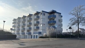 Un immeuble résidentiel à plusieurs étages, doté de balcons, d’un espace de stationnement et surplombant un ciel dégagé.