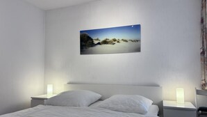 Une chambre à coucher comprenant un lit, deux tables de chevet avec des lampes, une petite table et un tableau accroché au mur.
