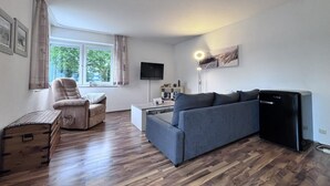 Un salon comprenant un canapé, un fauteuil, un téléviseur et un petit réfrigérateur noir.