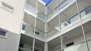 Un edificio de varios pisos con fachada de vidrio, varios balcones y un patio con una pequeña fuente.