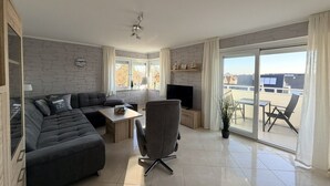 Una sala moderna con sofá, televisión, mesa de comedor y balcón con sillas.