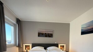 Un dormitorio moderno con una cama doble, dos mesitas de noche con lámparas, una luz de techo, una ventana con cortinas y un cuadro en la pared.
