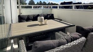 A balcony with a table and chairs, a glass door, and a view of buildings and trees. - House Poseidon, vacation apartment POS20 incl. beach chair (Cuxhaven)