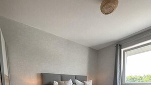 A modern bedroom with a grey bed, bedside tables, and a large window with a view. - House Poseidon, vacation apartment POS20 incl. beach chair (Cuxhaven)