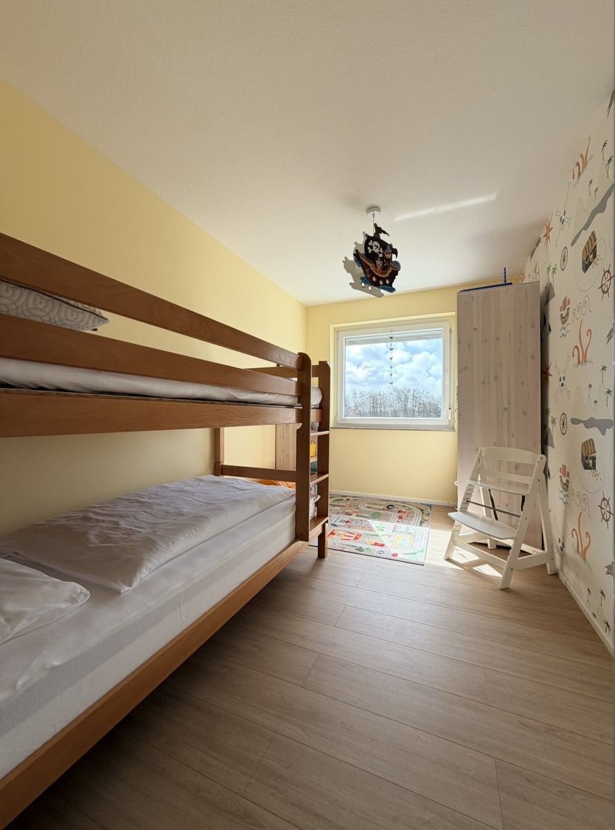 A bunk bed room with a window, a ceiling fan, and a wall with nautical-themed wallpaper.