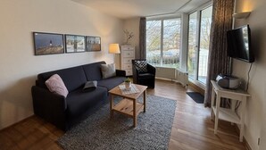Ein modernes Wohnzimmer mit einem dunklen Sofa, einem Holztisch und einem Fernseher auf einem Lowboard.