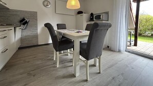 Ein Essbereich mit Tisch und Stühlen, einer Pendelleuchte, einer Uhr und Blick ins Freie.