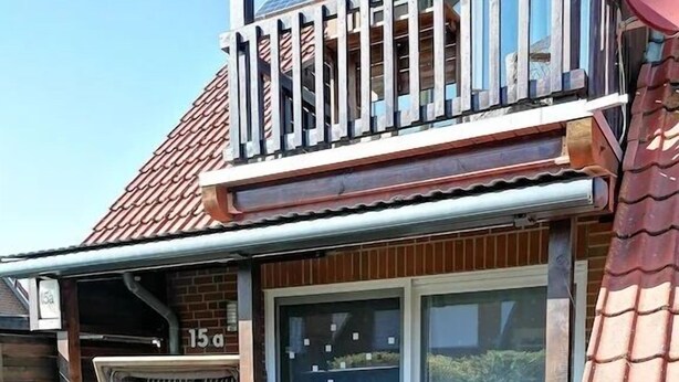 Eine Terrasse mit Tisch und Stühlen, eine integrierte Sitzbank mit Kissen und eine Schiebetür aus Glas.