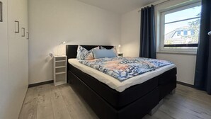 Ein modernes Schlafzimmer mit einem schwarzen Bett, einem Nachttisch mit Lampe und einem Fenster mit Vorhängen.