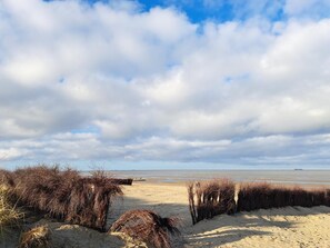 A beach with sand dunes and a wooden pier extending into the water. - Poseidon House, Apartment POS07 (Cuxhaven)