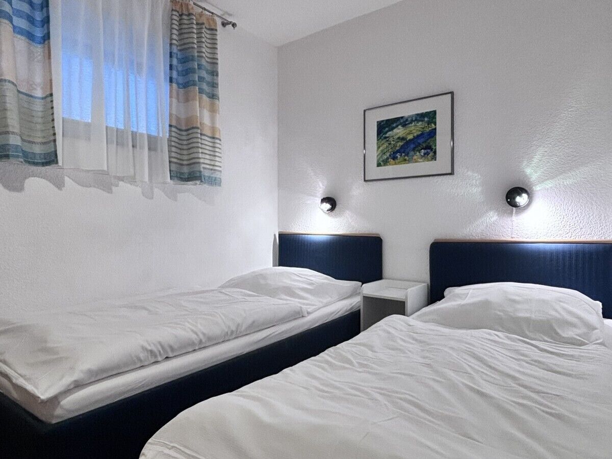 A hotel room with two single beds, a nightstand, a wall-mounted lamp, and a framed picture.