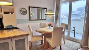 Un comedor con una mesa redonda, cuatro sillas, un florero con flores, un espejo y una lámpara.