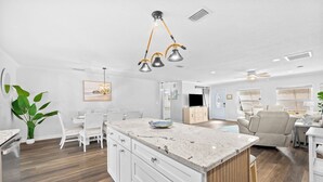 Cucina spaziosa con isola centrale grande, mobili bianchi e lampada a sospensione moderna.