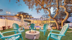 Un giardino sul retro con un focolare, posti a sedere all'aperto e luci decorative.