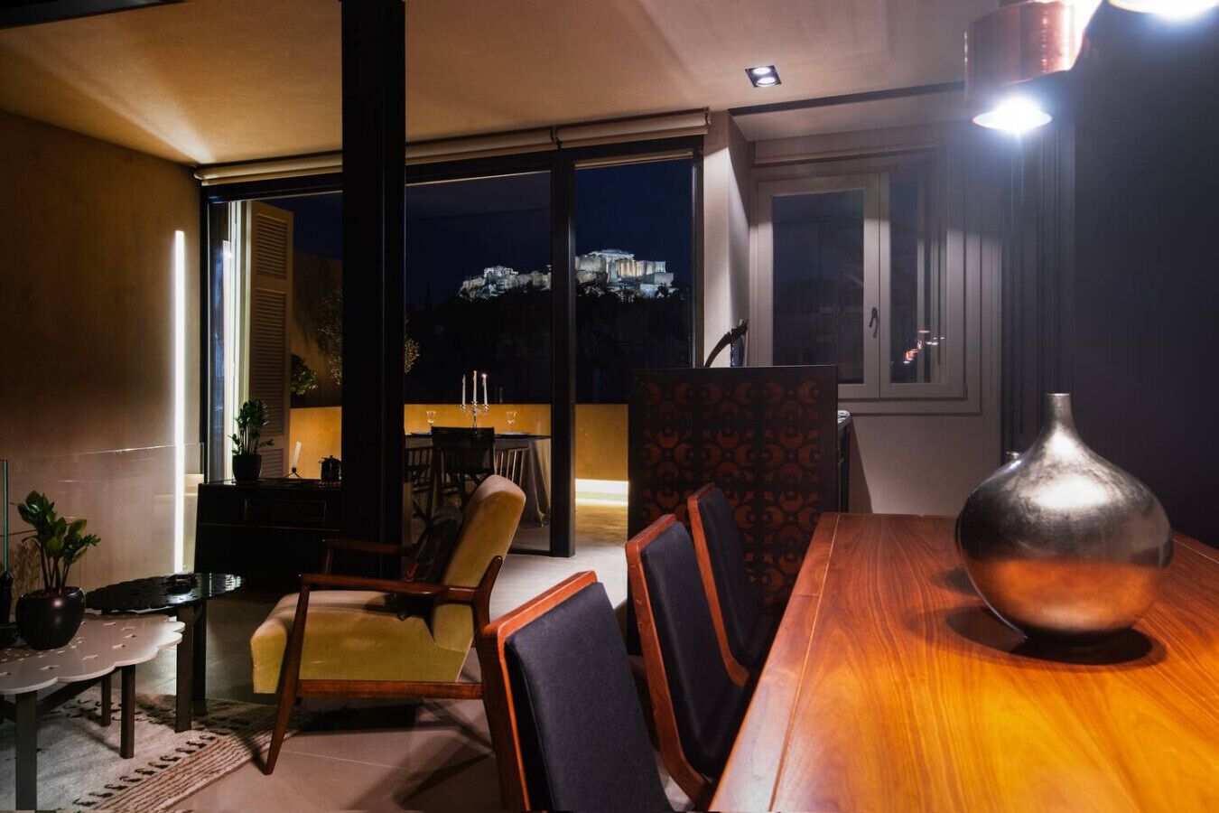 Un comedor con una mesa y sillas de madera, un jarrón y vistas a un paisaje urbano nocturno.