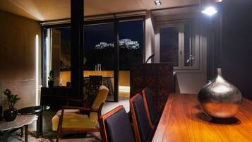 Un comedor con una mesa y sillas de madera, un jarrón y vistas a un paisaje urbano nocturno.