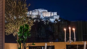 En vy över Akropolis under natten, med ett bord och några stolar i förgrunden.