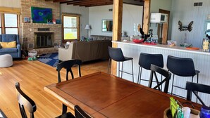 Ein geräumiges Wohnzimmer mit Kamin, eine Essecke mit Holztisch und -stühlen sowie ein Küchenbereich mit Bar.