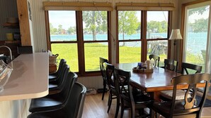 Ein Essbereich mit Holztisch und -stühlen, großen Fenstern mit Seeblick und einer Küchenzeile mit Spüle und Schränken.