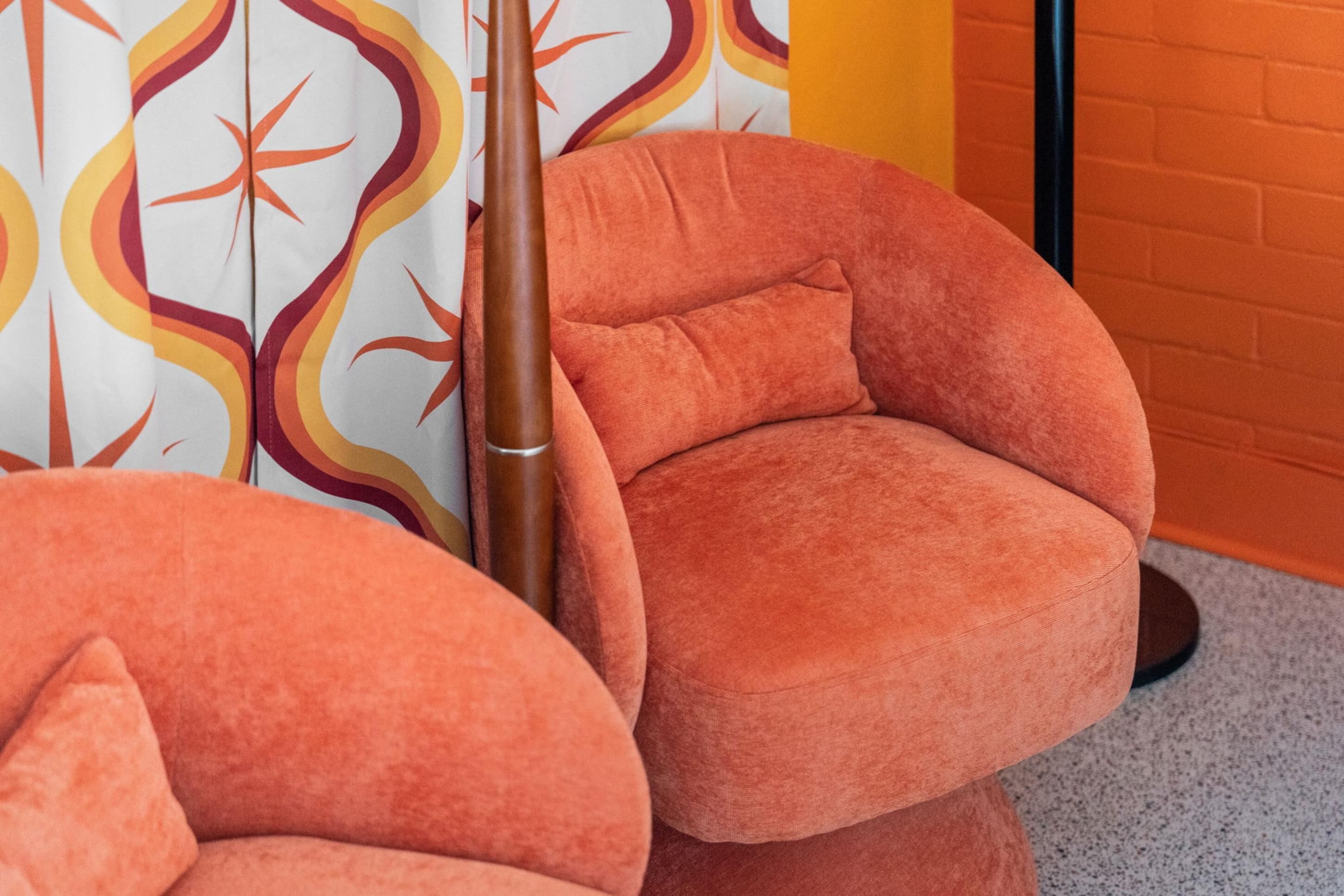 Una habitación con dos sillones tapizados en naranja y una cortina estampada.